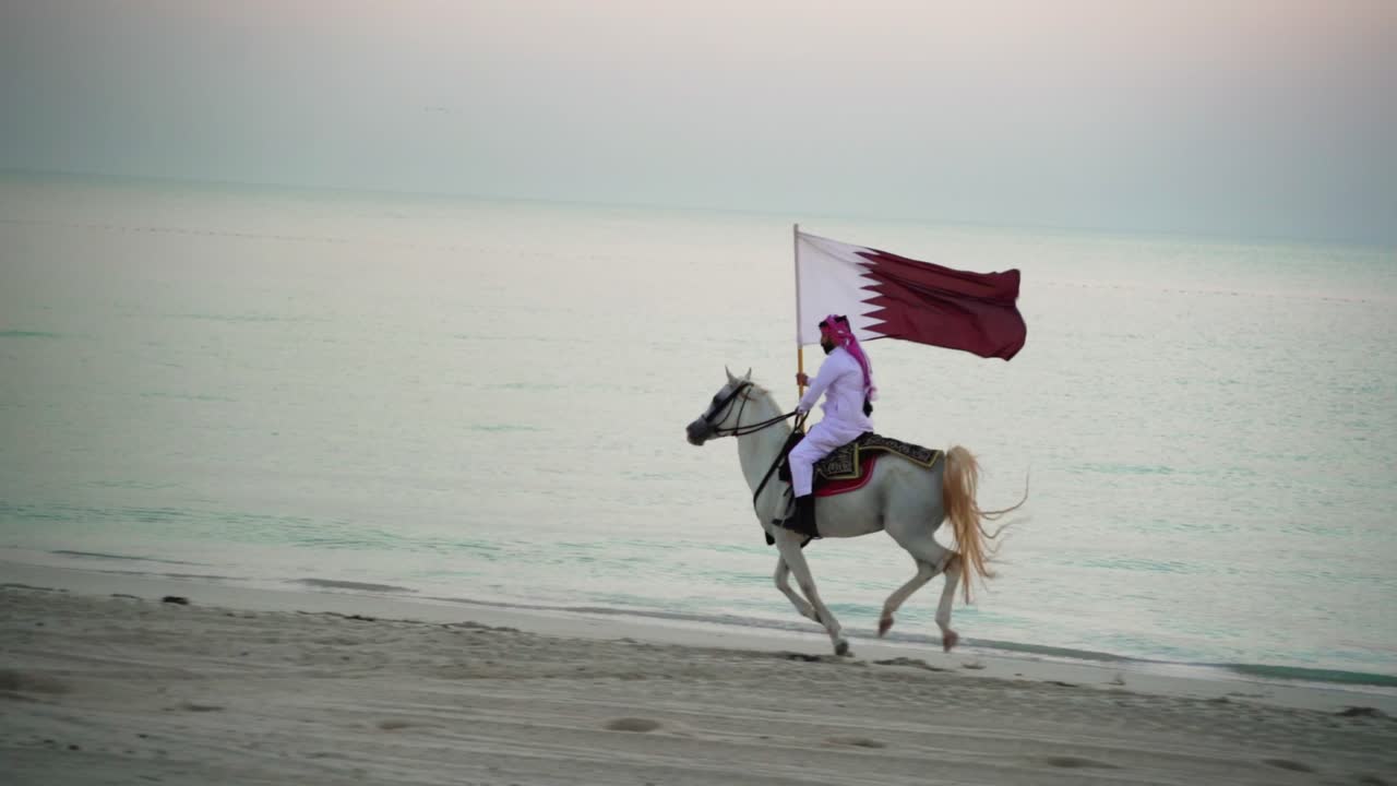 un caballero montando un caballo corriendo y sosteniendo la bandera de qatar cerca del mar-1