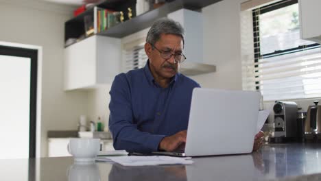 Senior-mixed-race-man-using-laptop-in-kitchen