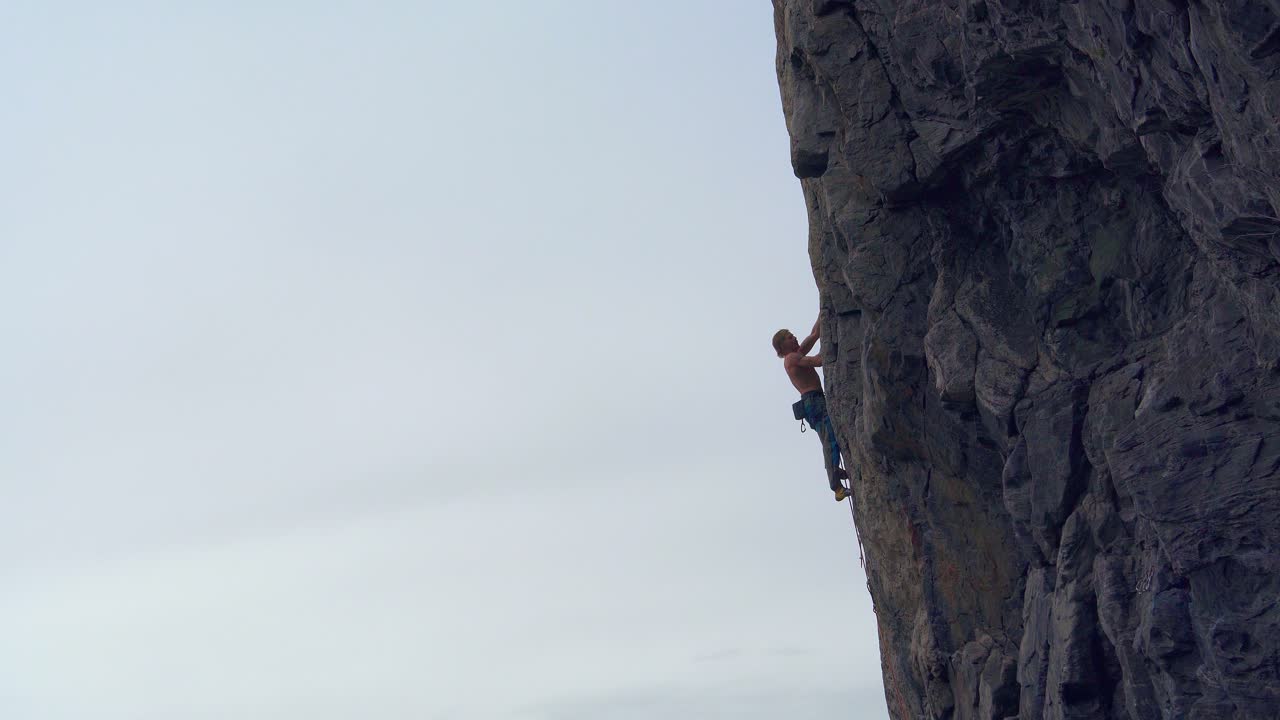 Mountaineer rappelling down a large mountain without a shirt