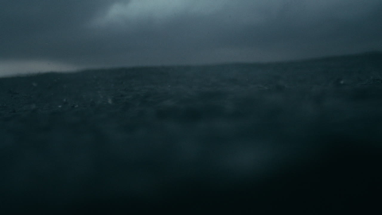 Moody storm cloud reflections and raindrops hitting ocean in abstract rhythm