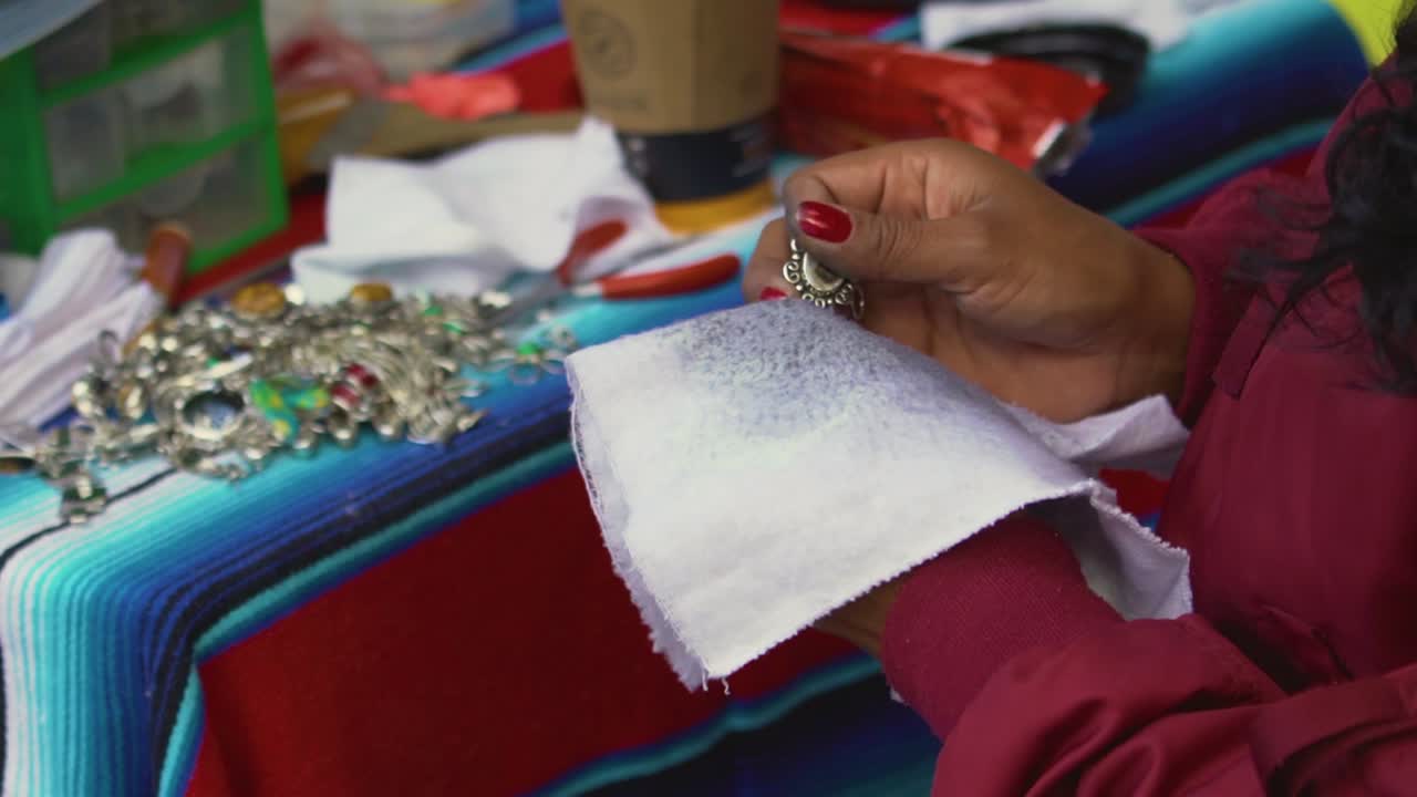 Handheld close up of an indigenous woman waxing her handcrafts getting them ready for sale