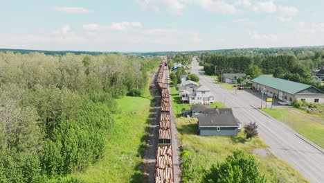 drone shot ascending over a long stationary freight train carrying lumber in rural maine