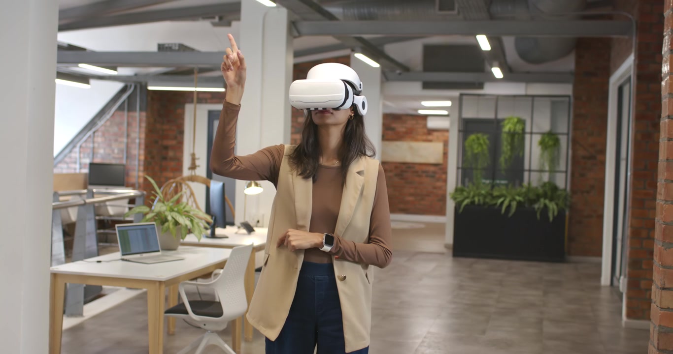 Donna afroamericana che regola un visore VR bianco, alzando un dito e selezionando elementi in ufficio.