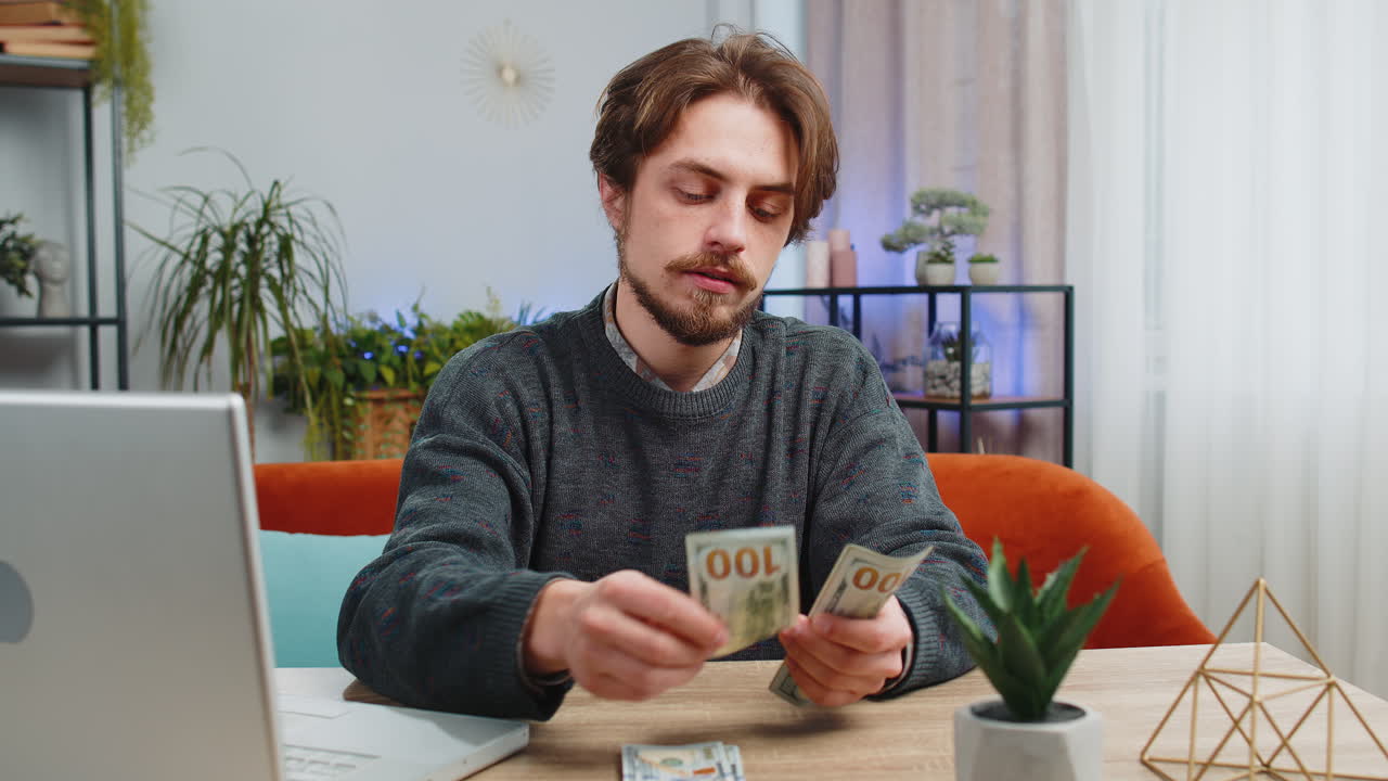 웃는 행복한 남자가 돈을 계산하고 현금과 노트북 pc를 사용하여 가정 소득을 계산합니다.