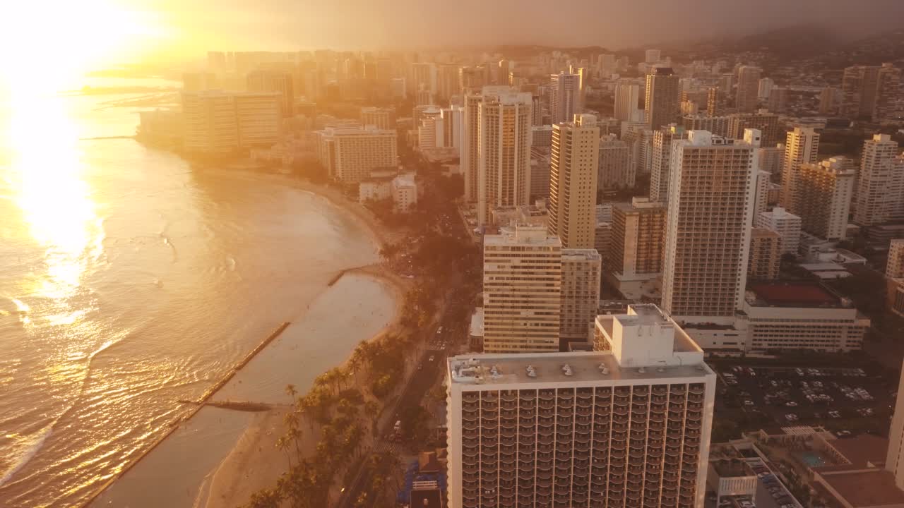 Drone aéreo panorâmico voando lentamente sobre o colorido horizonte de Honolulu durante o pôr do sol em Oahu, Havaí, com a Praia de Waikiki como um ponto de interesse especial