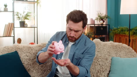 man shaking piggy bank counting collected coins saving money checking personal finances at home