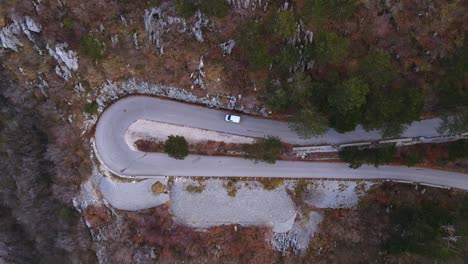 car drives on loop of winding asphalt road on mountain slope with thickets and green trees at sunlight in spring aerial panorama