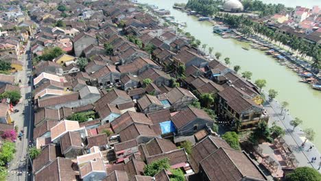 drone aerial view in vietnam flying over hoi an brown color river canal in the city, small brick houses and wooden boats on a sunny day