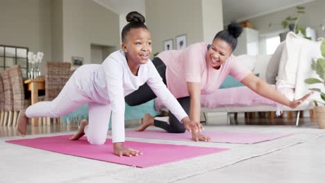 happy unaltered african american mother and daughter doing yoga stretching at home, slow motion