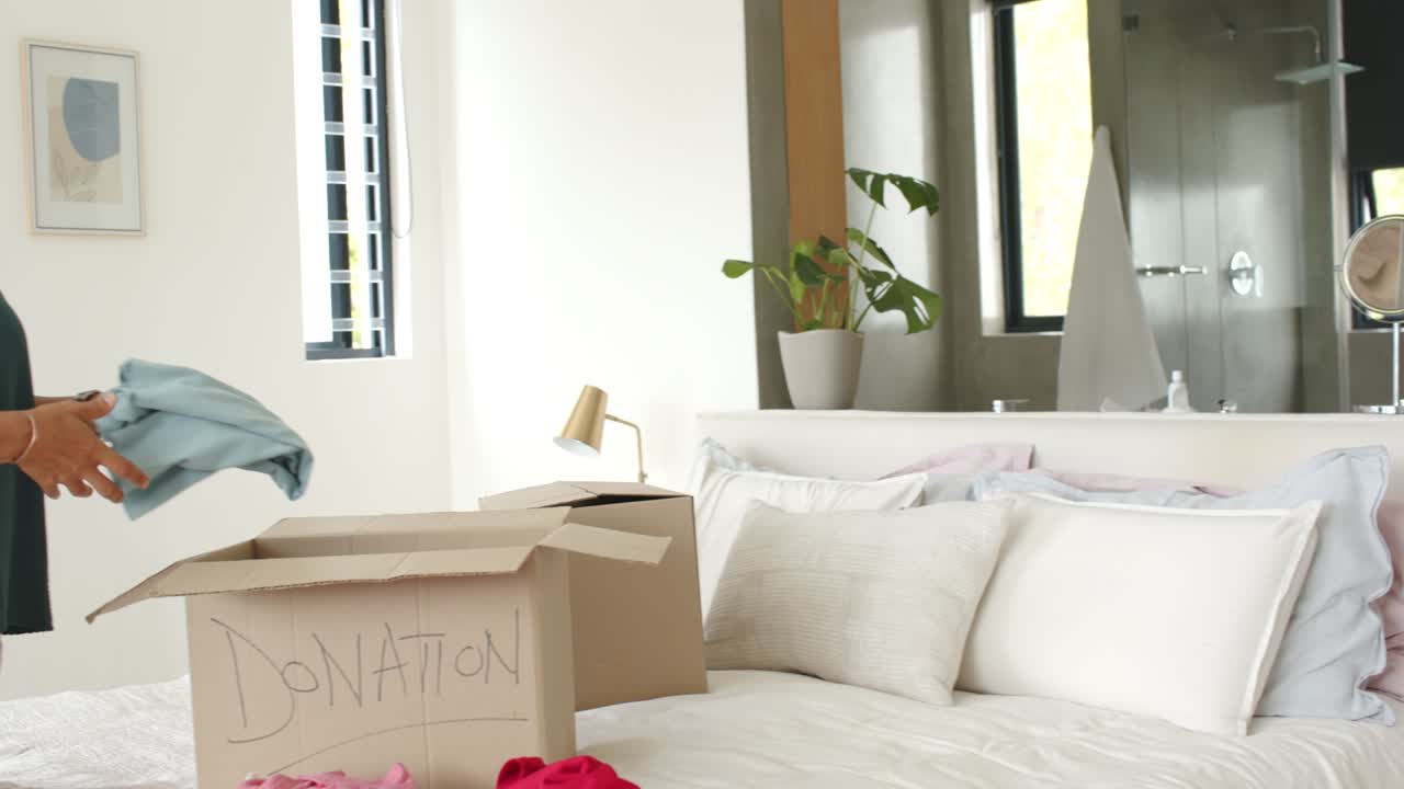 Uomo anziano e donna di mezza età che preparano una scatola per donazioni in camera da letto, maneggiando una camicia a quadri blu.