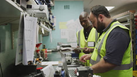 Un-Caucásico-Y-Un-Afroamericano-Trabajadores-De-Fábrica-De-Pie,-En-Discusión,-Usando-Una-Computadora-L