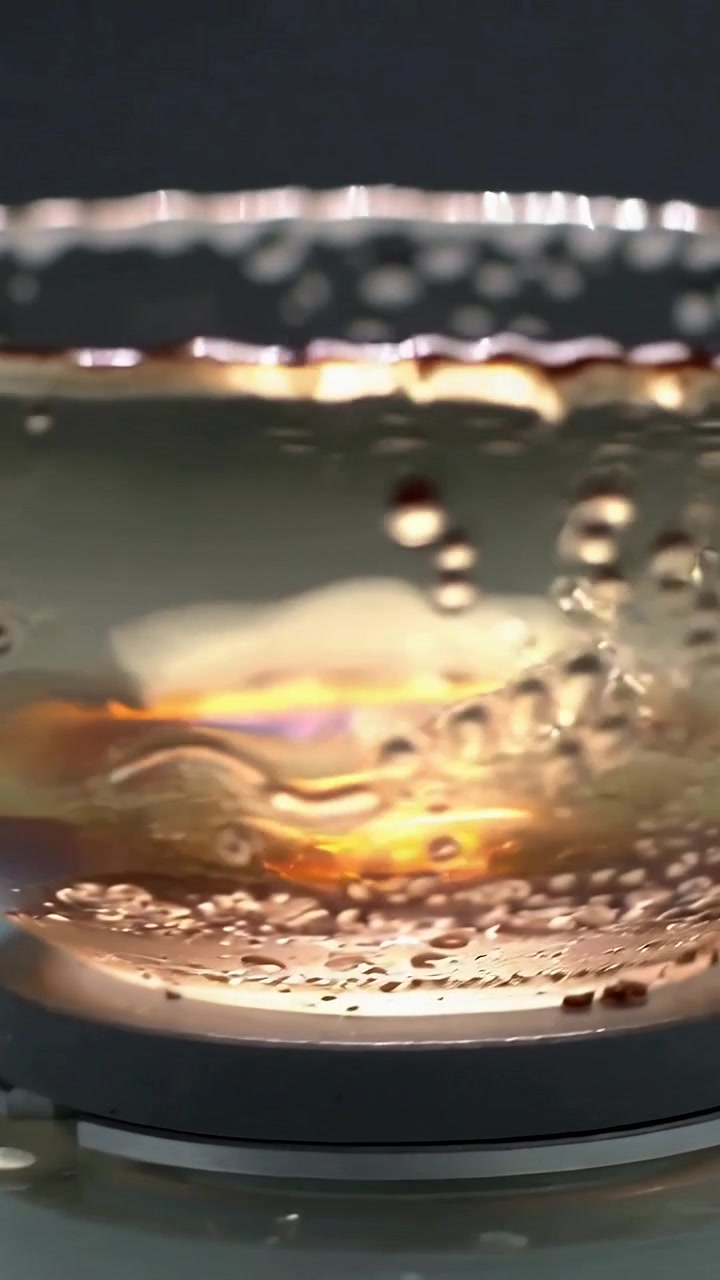 Vertical video: Heating base warming glass on counter, heating liquid and forming bubbles and beads