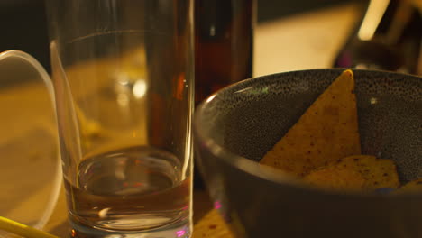 Close-Up-Of-Half-Empty-Spirit-Glasses-With-Beer-Bottles-And-Snacks-On-Table-After-House-Party