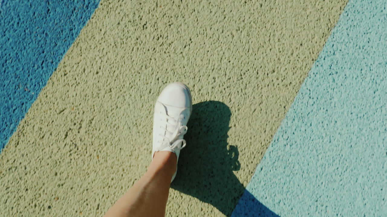 Vista in prima persona di piedi con scarpe sportive che camminano su asfalto colorato e variegato.