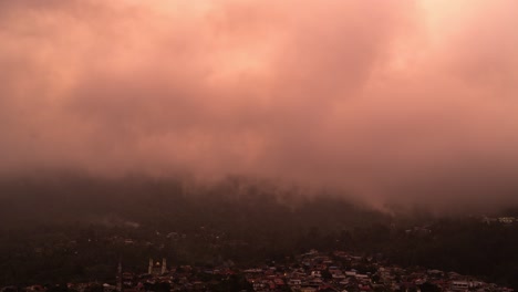 village and mosque at the base of misty mountains under changing sky