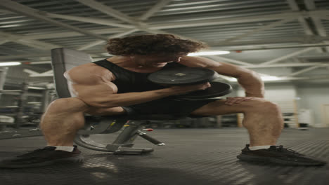 muscular man performing seated bicep curls with dumbbell in gym