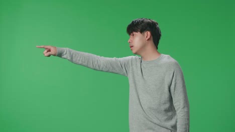 side view of an angry asian man scolding while standing on green screen in the studio