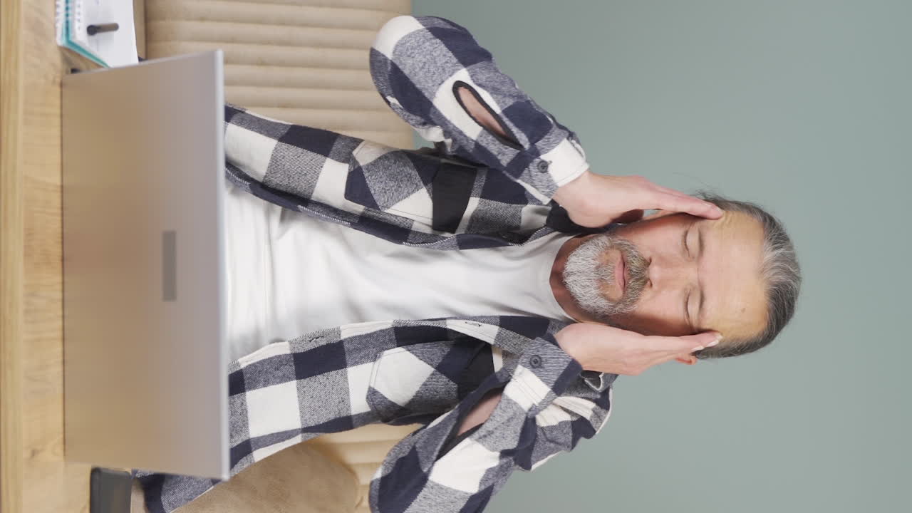 el video vertical del anciano trabajando en la computadora portátil tiene dolor de cabeza.