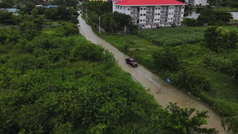 Imágenes-Aéreas-De-Un-Camión-Que-Viaja-A-Través-De-Las-Sucias-Aguas-De-Inundación-De-Un-Pueblo-En-Tailandia-Después-De-Fuertes-Lluvias