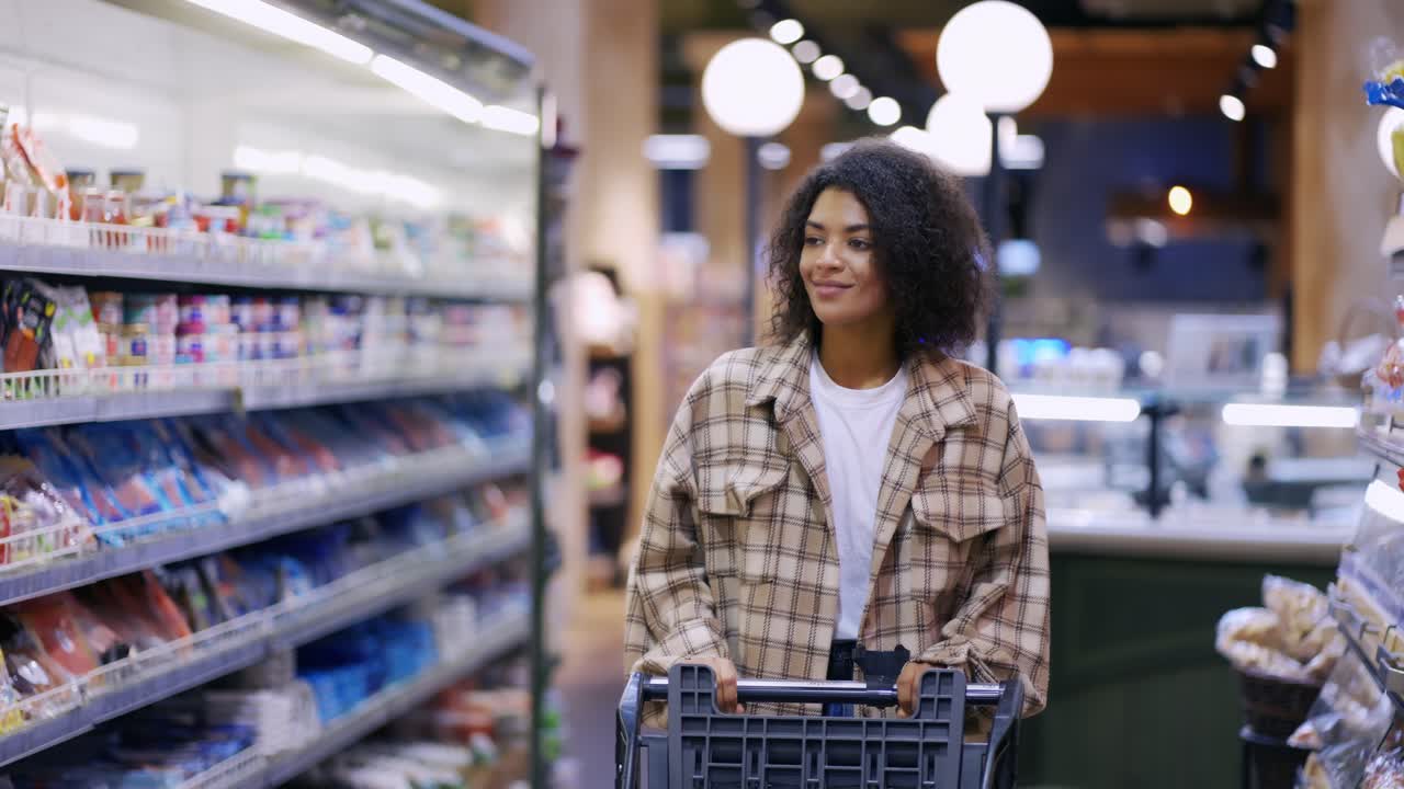 una mujer afroamericana sonriente camina por el supermercado con un carrito