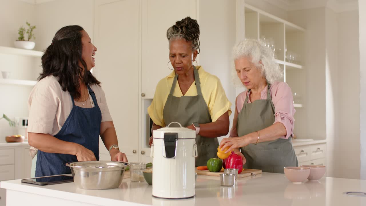 Diverse Frauen schneiden Paprika, öffnen ein Gerät, teilen eine Karotte und bereiten eine Mahlzeit an der Kücheninsel zu.