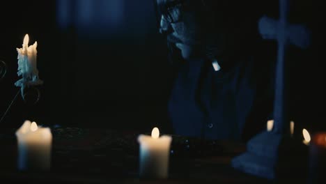 close up video capturing a priest sitting at the table anxiously looking around with a candlestick - close up video capturing a priest sitting at the table, anxiously looking around with a candlestick in his hand, then taking a book and reading it carefully. creative content, halloween themed