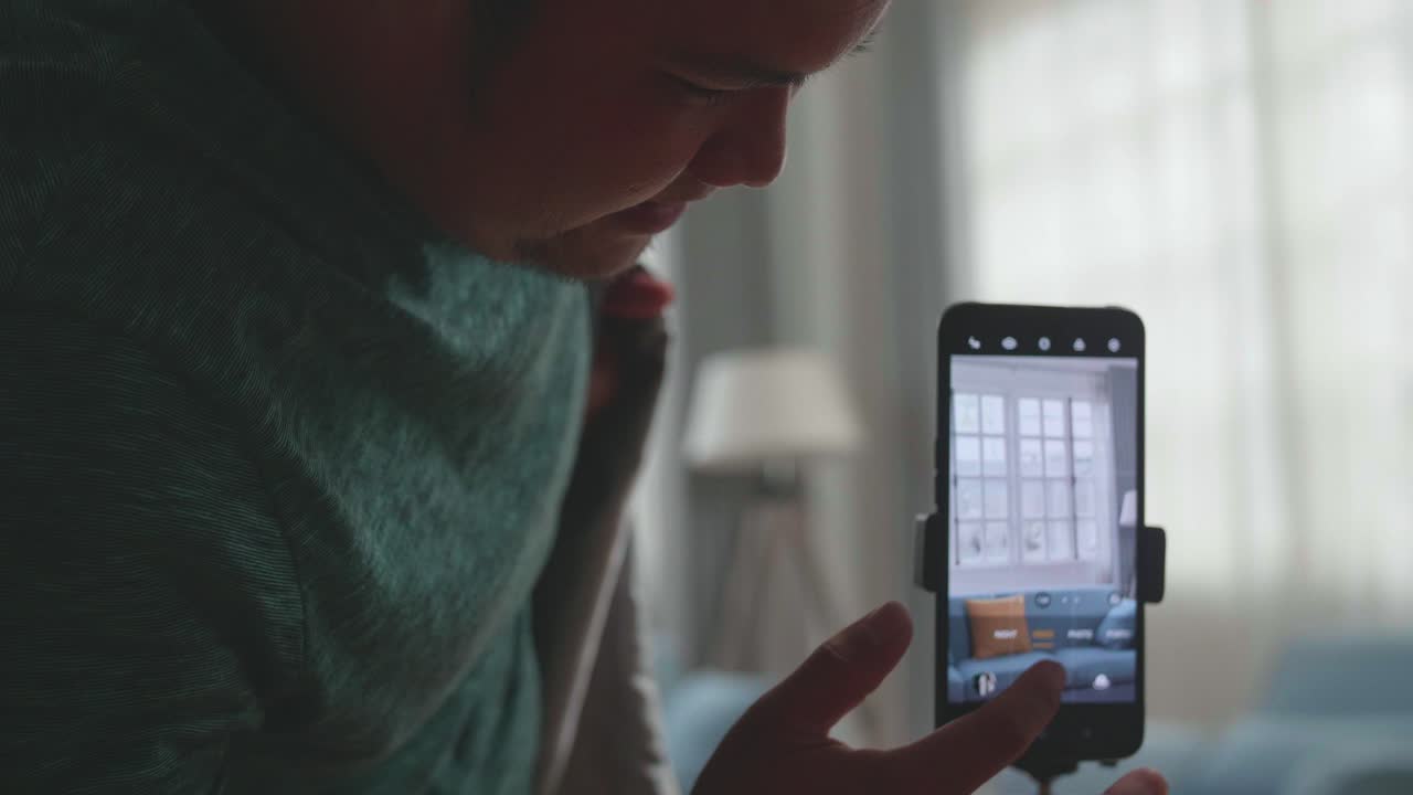 Display Smartphone Of Asian Man Shows Trick With Disappearing On Mobile Phone Camera While Recording Video Content For Social Networks In Cozy Room