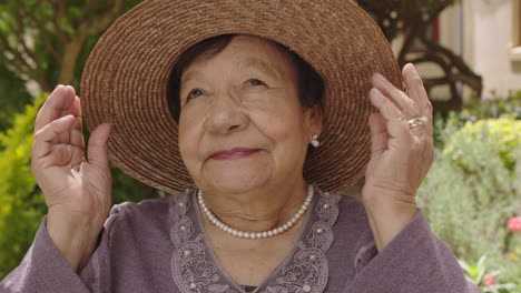 retrato de una hermosa anciana en el jardín sonriendo mirando hacia arriba con un collar de perlas de sombrero