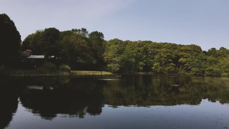 Beautiful-New-England-Pond-Aerial-Flying-Forward,-People-Walking-in-Background