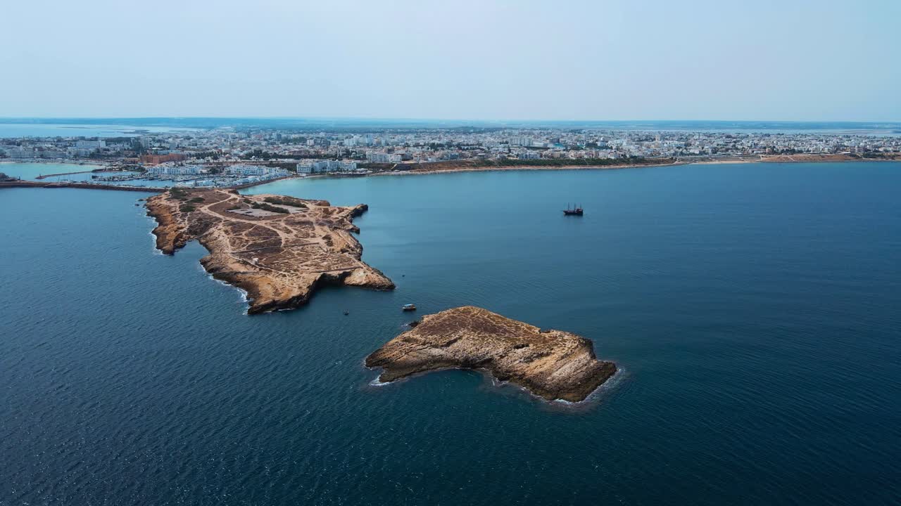 Land is jutting out of the ocean and houses are situated on it. along with boats floating nearby. It appears to be a place of interest for tourists due to its unique location.