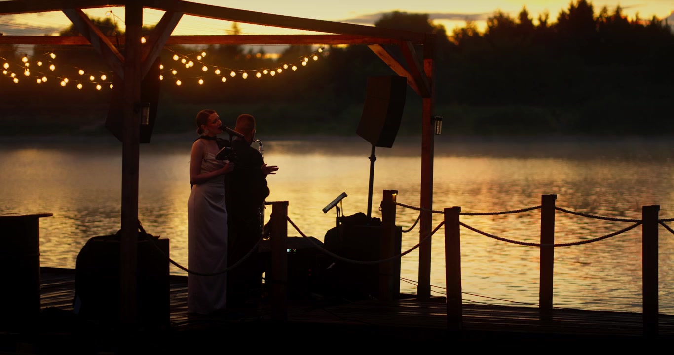 Duo musiziert auf einem See-Steg bei Sonnenuntergang