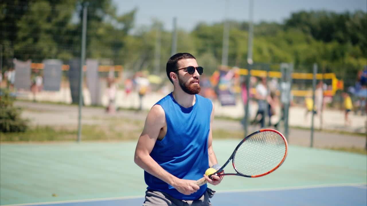 Man in blue shirt playing tennis on a blue and green court on a sunny day