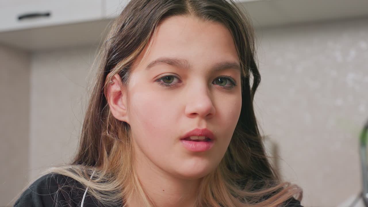 close up of calm woman seated in kitchen, natural light, relaxed expression, casual moment, domestic interior, youthful female, home atmosphere, candid, lifestyle, peaceful, indoors, day