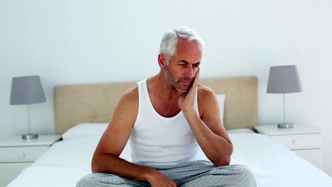 Hungover-man-sitting-on-the-end-of-his-bed-and-frowning