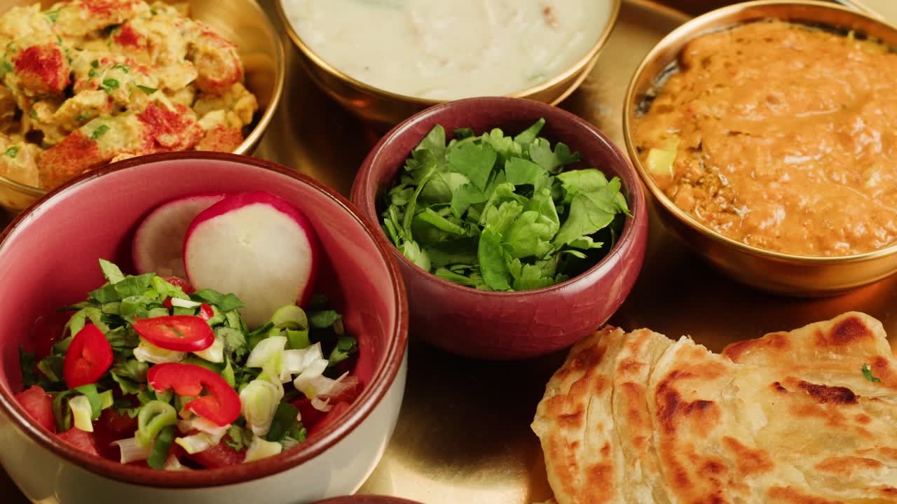 Assorted indian sri-lanka food set on wooden background. Dishes and appetisers of indeed cuisine, rice, lentils, paneer, samosa, spices, masala. Bowls and plates with indian food top view chicken. High quality 4k footage