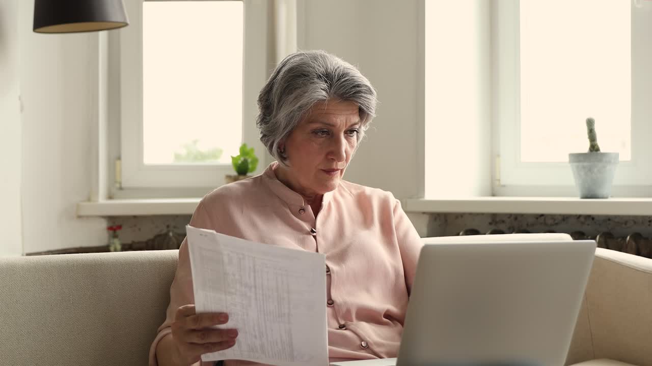 Old woman accountant review paper documents check payments on laptop