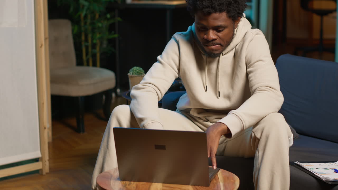 Focused man engaged in online research for a work project at home, sitting at his coffee table with laptop and reading articles on the internet. Person surfing webpages and gathering data. Camera A.