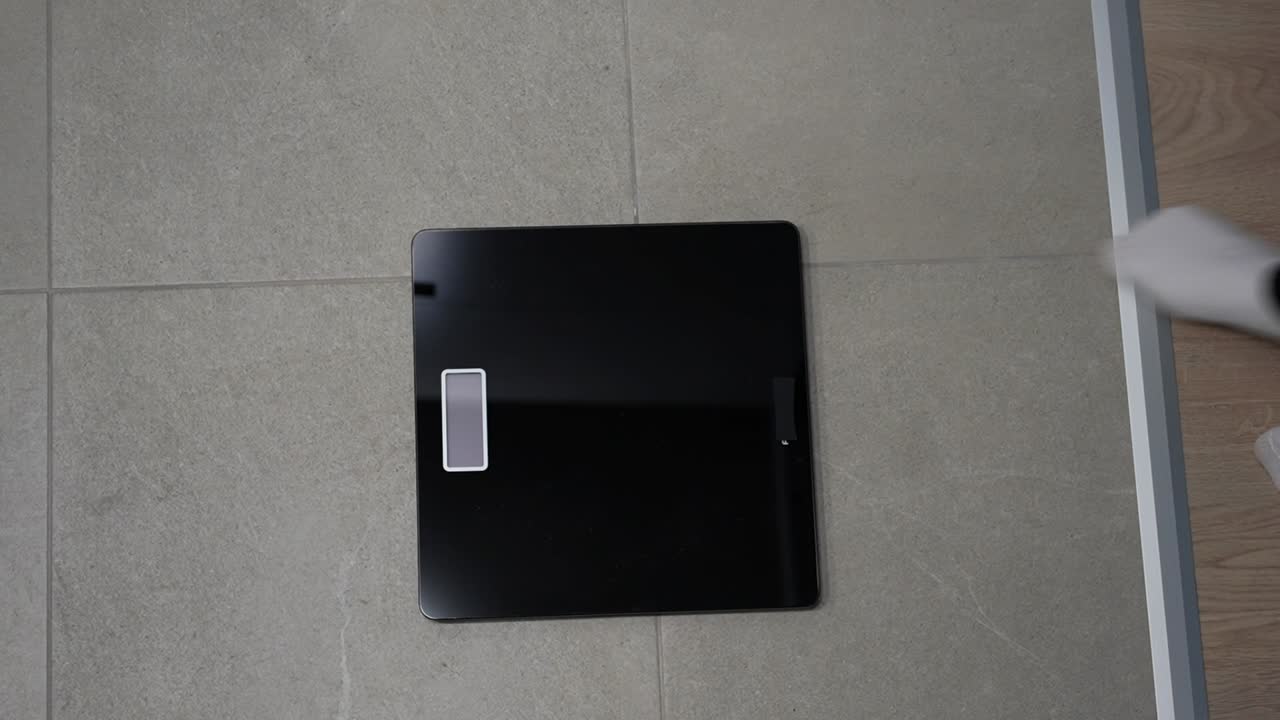 Top down view of a pregnant woman checking weight on a bathroom scale, focused on health monitoring