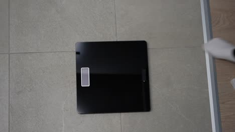 top down view of a pregnant woman checking weight on a bathroom scale, focused on health monitoring