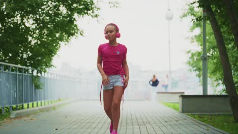 a young girl enjoys her music while walking in a green park, radiating joy and confidence as she listens to her favorite tunes and dances along the path