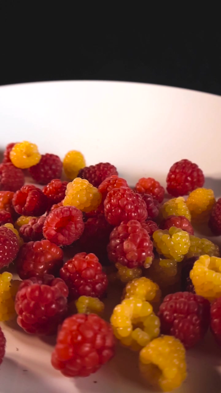 Delizioso piatto di lamponi freschi rossi e dorati che ruotano lentamente, offrendo una vista colorata e appetitosa del frutto maturo e sano su uno sfondo scuro in uno scatto macro ravvicinato