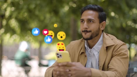 hombre sonriente sentado en una mesa al aire libre mirando un teléfono móvil con emojis de gráficos en movimiento que muestran múltiples notificaciones de redes sociales gustando y reaccionando al contenido en línea