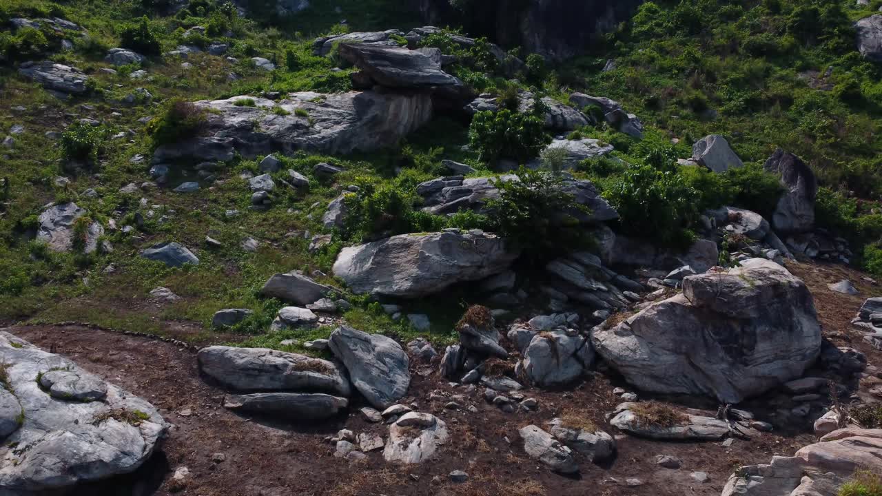 Boulders and scattered rocks in grassy patchy terrain captured from low altitude aerial, natural backdrop