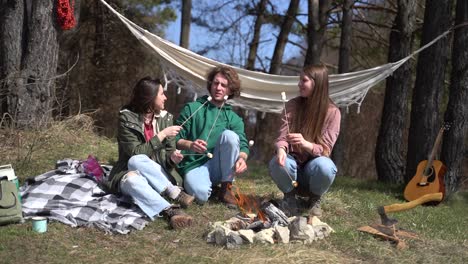 dos niñas y un niño calientan malvaviscos en una hoguera en el bosque.