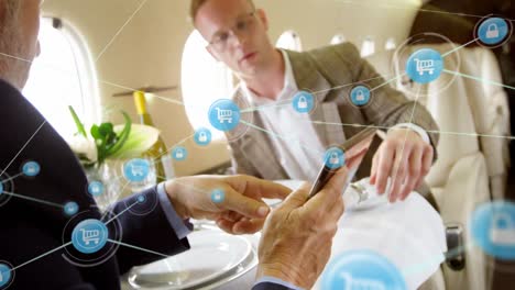 animación de una red de iconos digitales sobre dos hombres de negocios caucásicos usando una tableta digital en un avión