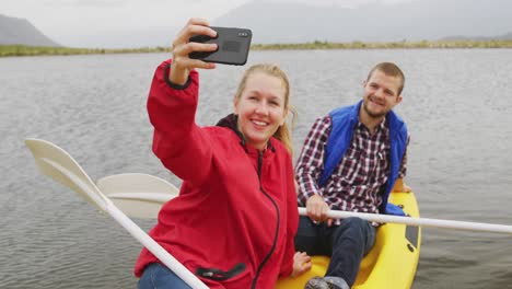 caucasian couple having a good time on a trip to the mountains, kayaking together on a lake, taking