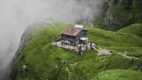 slow motion panning right shot of an old wooden chalet placed on a mountain cliff with mist in the background