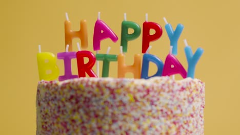 foto de estudio de pastel de cumpleaños giratorio cubierto con decoraciones y velas que deletrean feliz cumpleaños 3