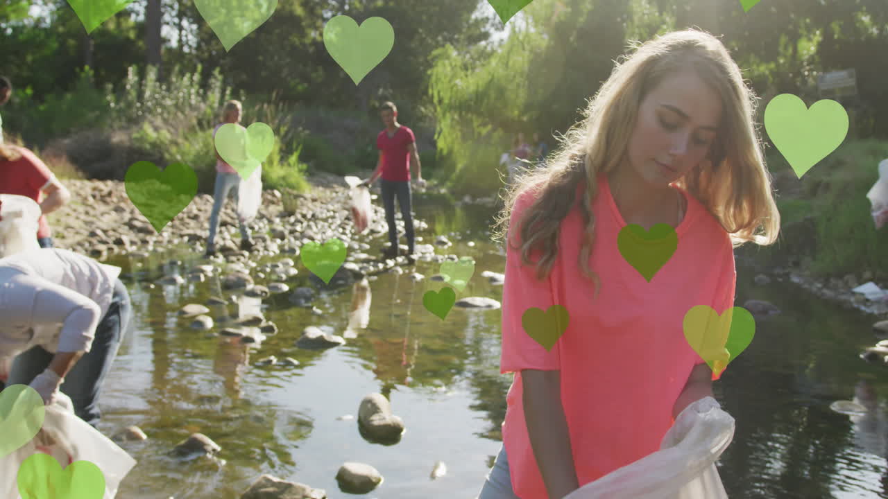 анимация зеленых сердец над разнообразной счастливой группой, собирающей мусор в сельской местности