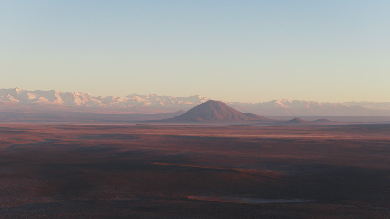 Aerial view of Volcán Diamante rising from the plains with the snow-covered Andes Mountains in the background during sunrise in Mendoza, Argentina.